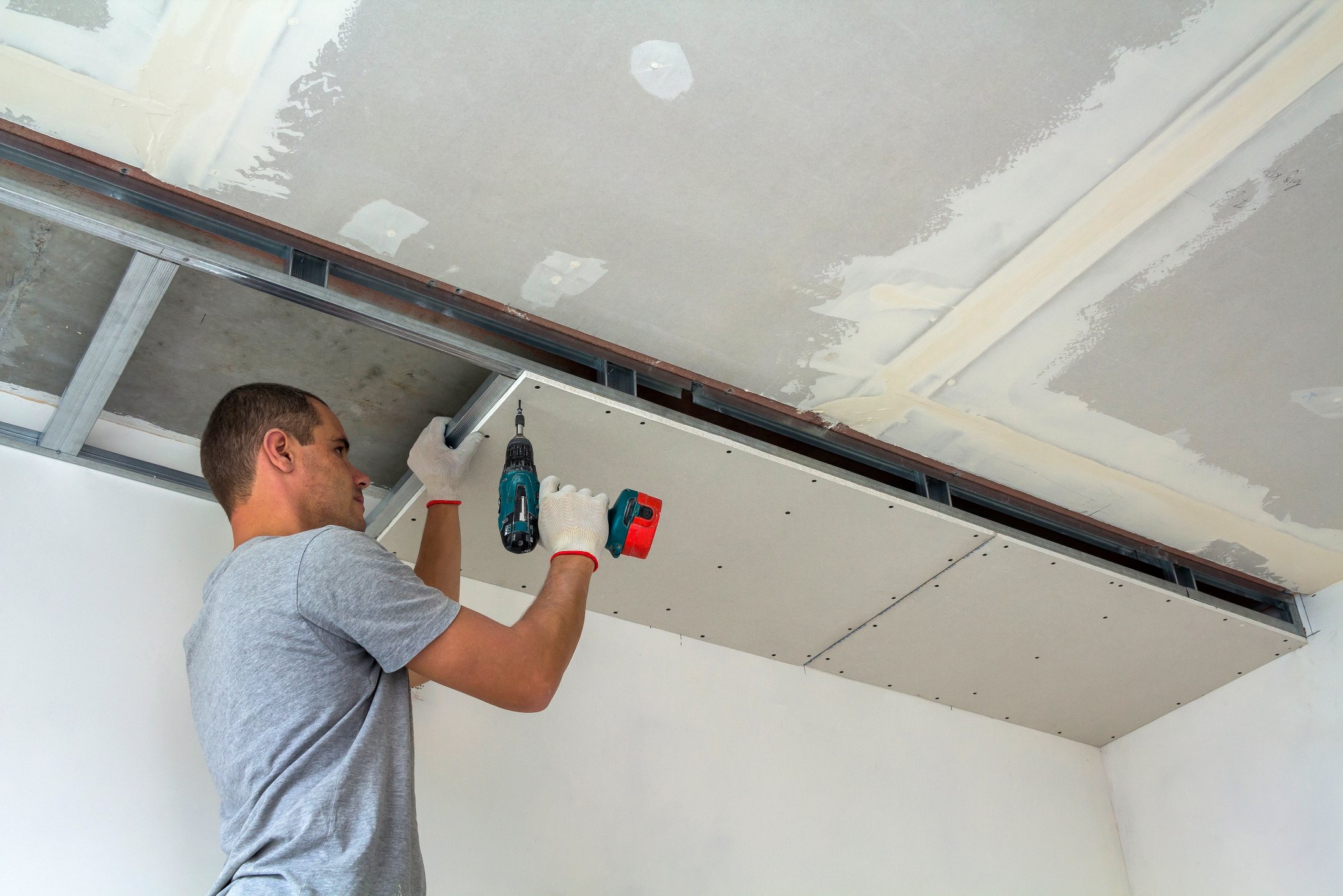 A man is working on drywall repair installation on a ceiling in a room 1