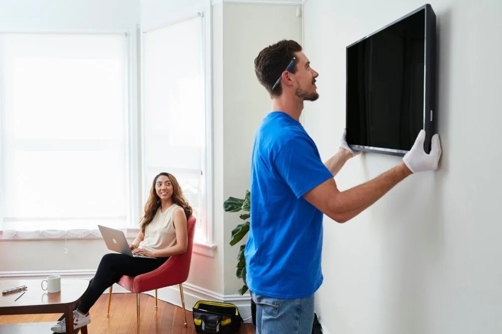 a man is installing a tv mount while lady is sitting nearby watching him