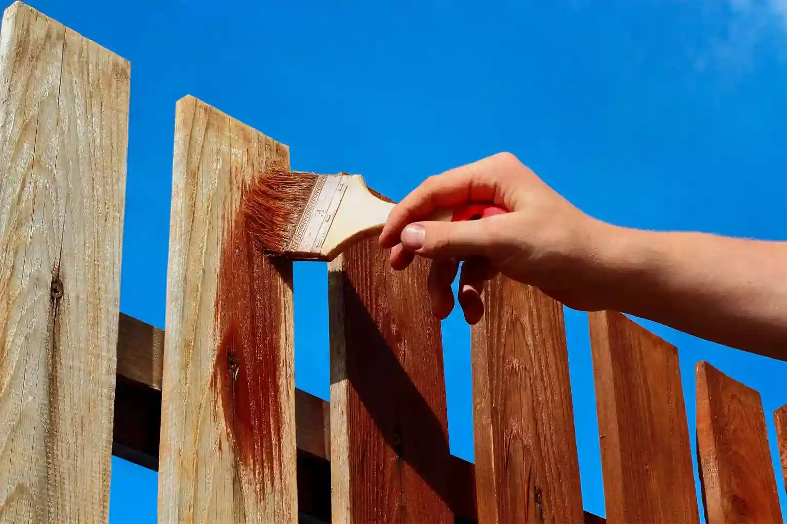 A worker is painting a fence